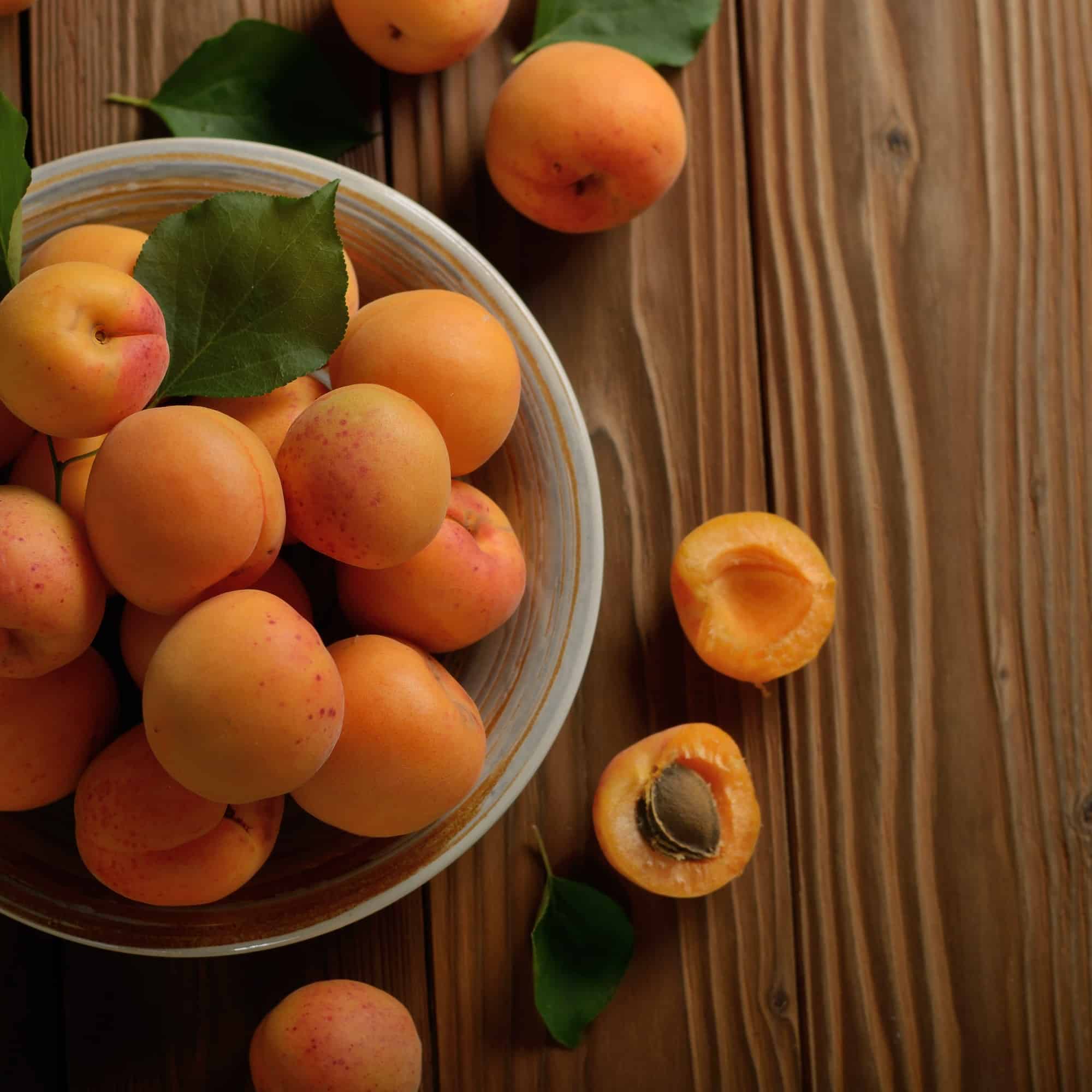 Top view of Clay dish full of ripe apricots on wooden table